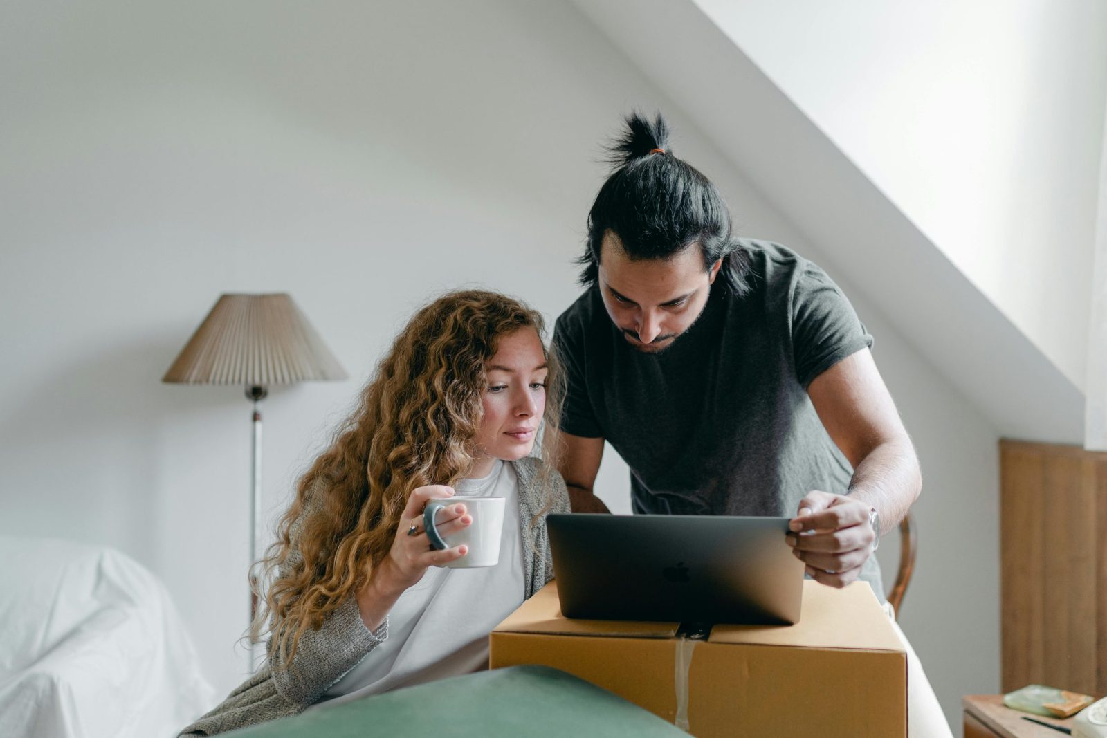 Concentrated young couple in casual outfit browsing netbook and packing stuff into carton boxes and suitcases to move out